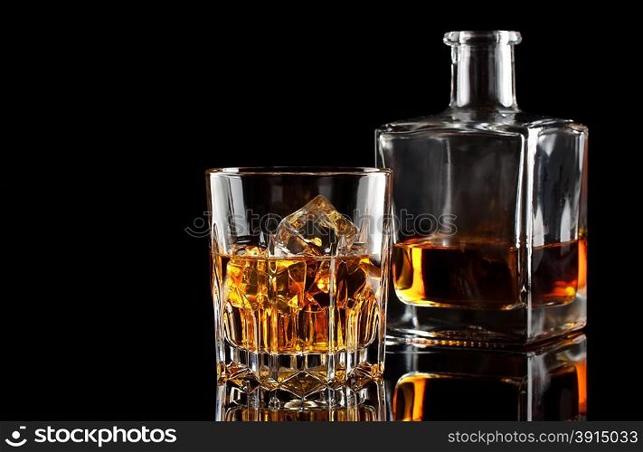 Glass of whiskey with ice and a square decanter isolated on a black background