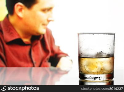 Glass of whiskey with ice and defocused male in the background