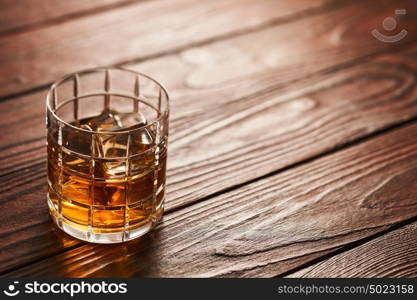 Glass of whiskey with ice cubes on rustic wooden table with copy-space