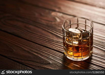 Glass of whiskey with ice cubes on rustic wooden table with copy-space