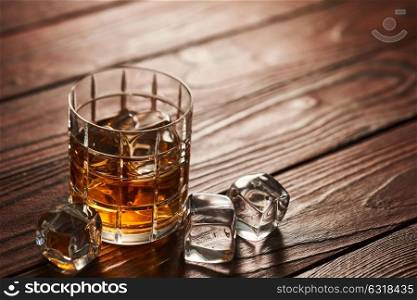 Glass of whiskey with ice cubes on rustic wooden table with copy-space