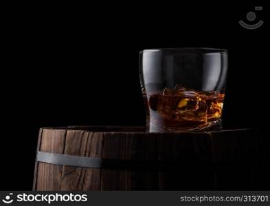 Glass of whiskey with ice cubes on top of wooden barrel. Cognac and brandy drink