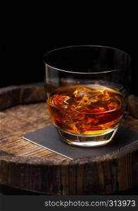 Glass of whiskey with ice cubes on top of wooden barrel. Cognac and brandy drink