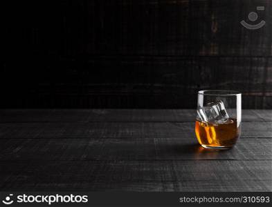 Glass of whiskey with ice cubes on wooden background