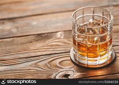 Glass of whiskey with ice cubes on wooden table. Glass of whiskey with ice cubes on rustic wooden table with copy-space