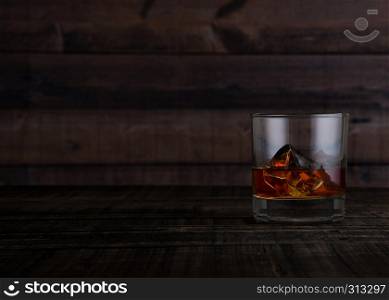 Glass of whiskey with ice cubes on wooden table background