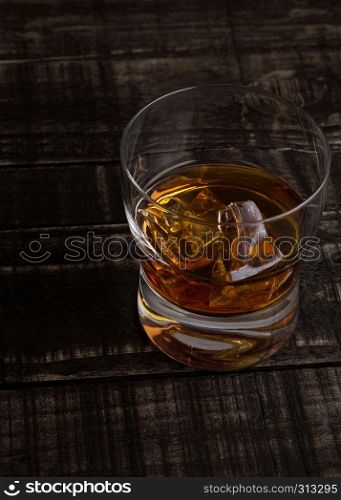Glass of whiskey with ice cubes on wooden table background top view