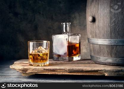 Glass of whiskey with ice decanter and barrel on wooden table. Glass of whiskey with ice decanter and barrel
