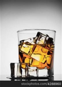 Glass of whiskey with ice melted on gradient background
