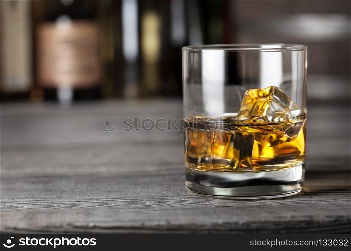 Glass of whiskey with ice on the bar rack shot with blurred background. Glass of whiskey with ice on the bar rack
