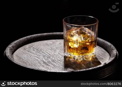 Glass of whiskey with ice on wooden barrel on black background. Glass of whiskey with ice on wooden barrel