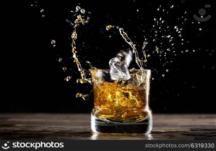 glass of whisky in a dark ambient with a ice cube falling making a splash