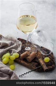 Glass of white homemade wine with corks, corkscrew and grapes on wooden board with linen cloth on light table background. Top view