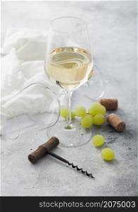 Glass of white refreshing wine with grapes and corkscrew on light table background.