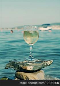 Glass of white wine by the coast.on the rocks, washed by the waves of the sea