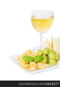 Glass of white wine, different varieties of cheese, green grapes and basil leaves on the white porcelain plate, isolated on white background