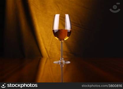 Glass of white wine over a draped background lit yellow