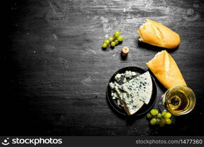 glass of white wine with blue cheese and ciabatta . On a black wooden background.. glass of white wine with blue cheese and ciabatta .
