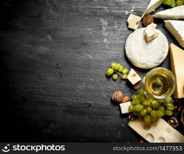 glass of white wine with different cheeses , grapes and nuts.On a black wooden background.. glass of white wine with different cheeses , grapes and nuts.