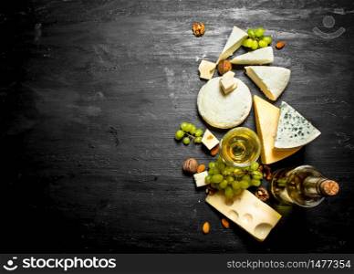 glass of white wine with different cheeses , grapes and nuts.On a black wooden background.. glass of white wine with different cheeses , grapes and nuts.