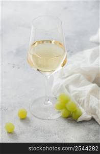 Glass of white wine with grapes and linen cloth on light table background.