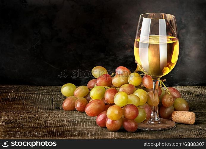 Glass of white wine with grapes on vintage wooden table