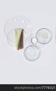 Glass petri dish with transparent pure serum for skin care with cosmetic tube on white background, top view. Concept laboratory tests and research, making and testing cosmetic. Glass petri dish with transparent pure serum for skin care