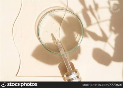 Glass petri dish with transparent pure serum with leaves shadows overlay for skin care on beige background, top view. Concept laboratory tests and research, making and testing cosmetic. Glass petri dish with transparent pure serum