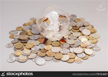 Glass piggy bank on coins isolated on gray