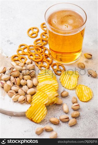 Glass pint of craft lager beer with snack on stone kitchen background. Pretzel and crisps and pistachio on roud wooden board