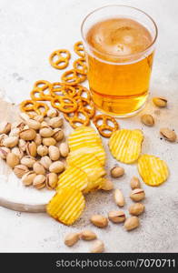 Glass pint of craft lager beer with snack on stone kitchen background. Pretzel and crisps and pistachio on roud wooden board