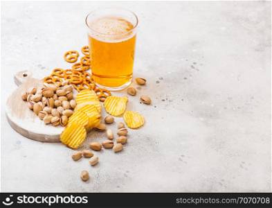 Glass pint of craft lager beer with snack on stone kitchen table background. Pretzel and crisps and pistachio on roud wooden board. Space for text.