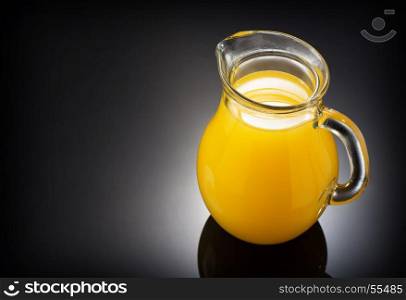 glass pitcher and orange juice on black background
