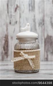 Glass round jars with linens, ribbons and birds on white wooden background