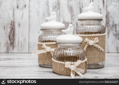 Glass round jars with linens, ribbons and birds on white wooden background