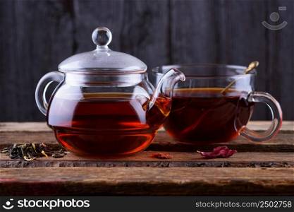 Glass teapot and cup with hot tea on wooden background dark still life