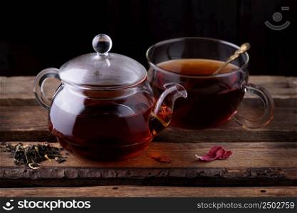 Glass teapot and cup with tea on wooden background dark still life