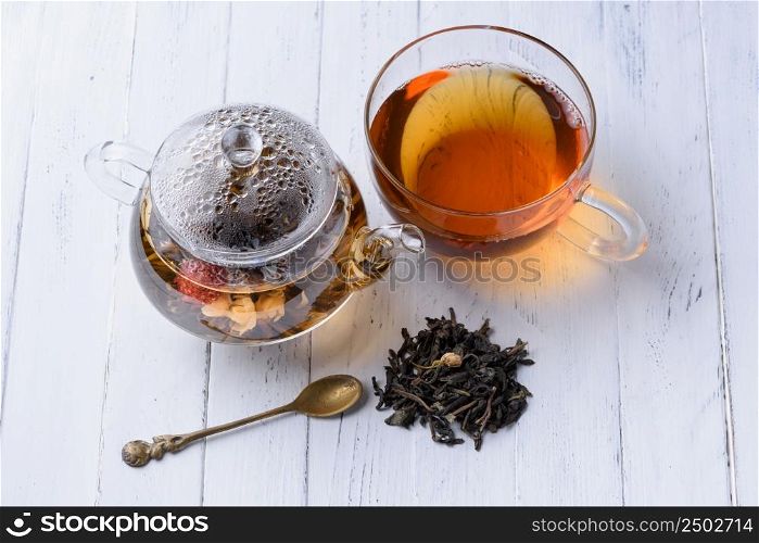 Glass teapot with blooming green tea and cup of tea on white wooden table still life