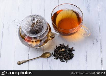 Glass teapot with blooming green tea and cup of tea on white wooden table still life