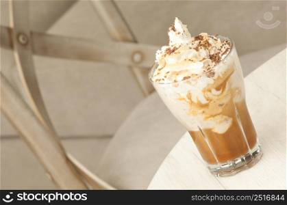 Glass transparent cup with ice cream milk shake on the table against the background of the chair closeup. a glass with a drink on the table