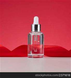 glass transparent white bottle with a pipette. Container for cosmetics, acids and oils on a red background