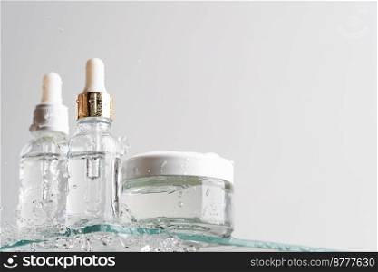 Glass tubes of cosmetic product with serum and cream on a glass shelf and water drops on a white background, bottom view. Skin care concept. Glass tubes of cosmetic