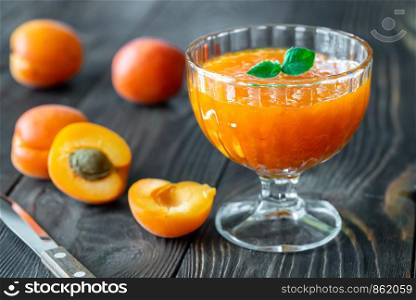 Glass vase of apricot jam with fresh apricots on the wooden background