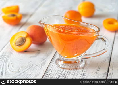 Glass vase of apricot jam with fresh apricots on the wooden background