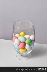 Glass vase with lots of small painted eggs on a gray background with copy space. Easter card layout. Multi-colored painted eggs in a glass vase on a gray background with space for text. Easter concept