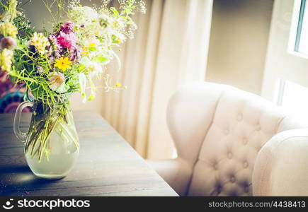 Glass vase with wild field flowers bunch on dinning table with chair at window. Floral home decoration