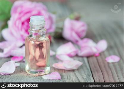 Glass vial with rose essential oil and flower of pink rose on a wooden background