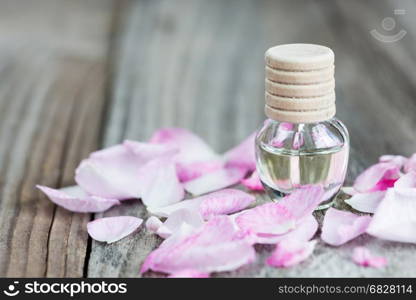 Glass vial with rose essential oil and petals of pink rose on a wooden background, with copy-space