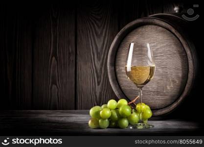 Glass white wine and bunch grapes on background of wooden barrels. Glass white wine and bunch grapes