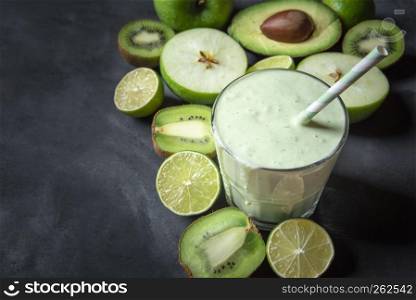 Glass with a fresh smoothie, surrounded by green fruits, on a kitchen table. Copy space on the left. Dieting food. Healthy eating. Vegetarian meal.